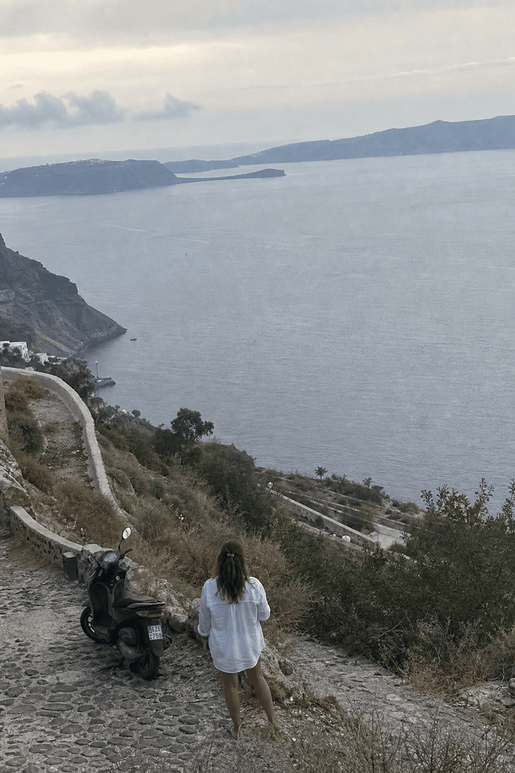 Debout de dos sur un sentier au-dessus de la caldeira, sous un ciel gris.